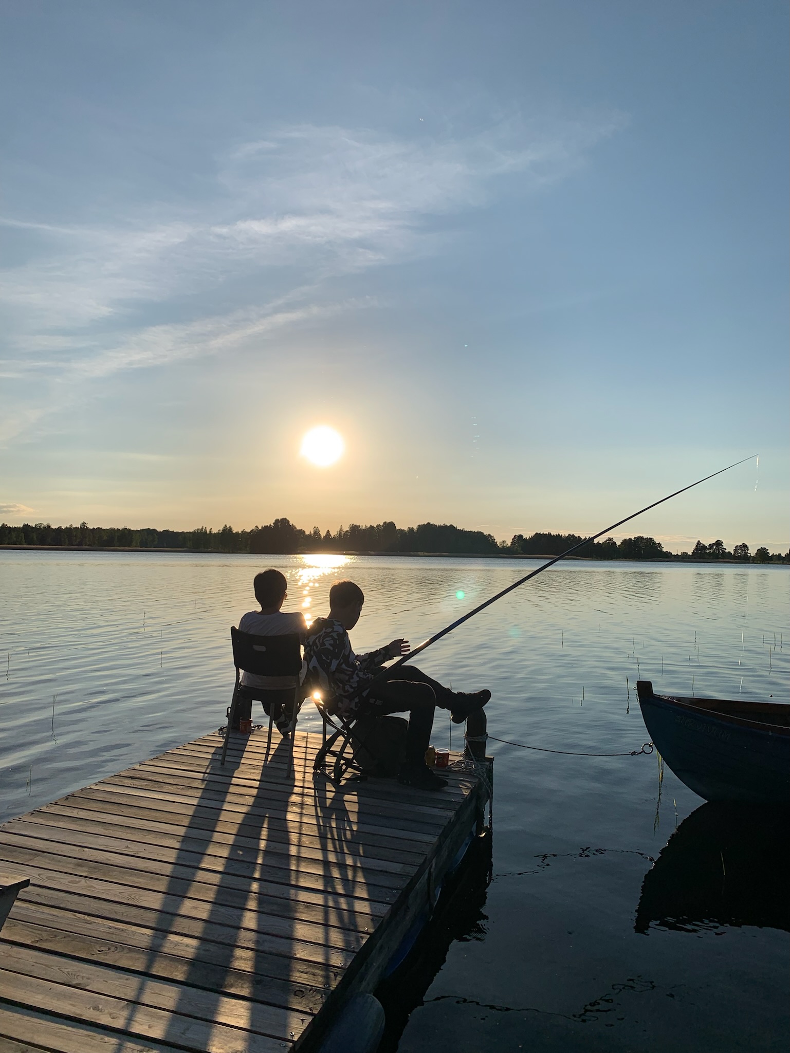 Två personer fiskar från bryggan i kvällssolen