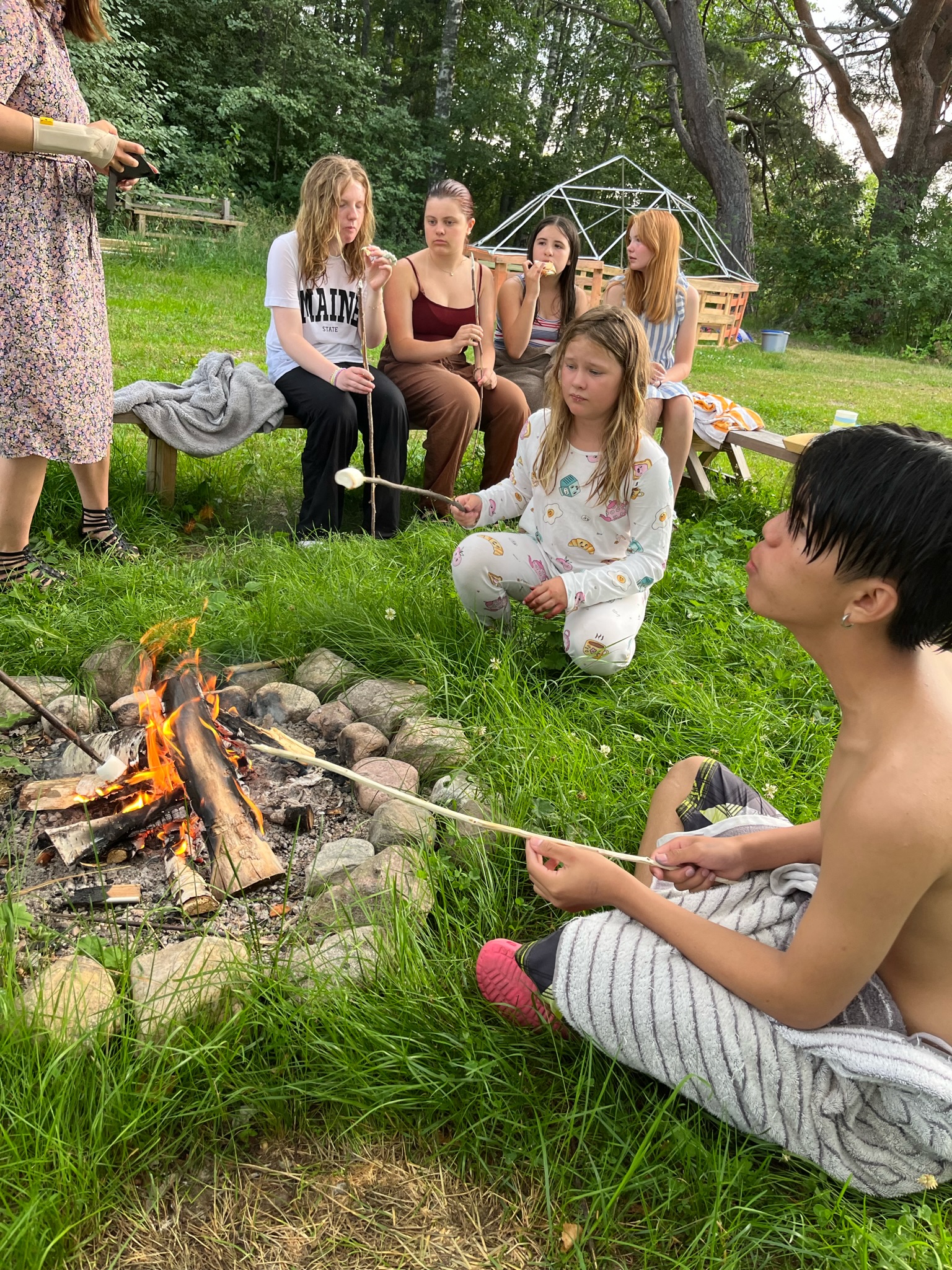 Deltagare samlas kring en lägereld på gräsmattan