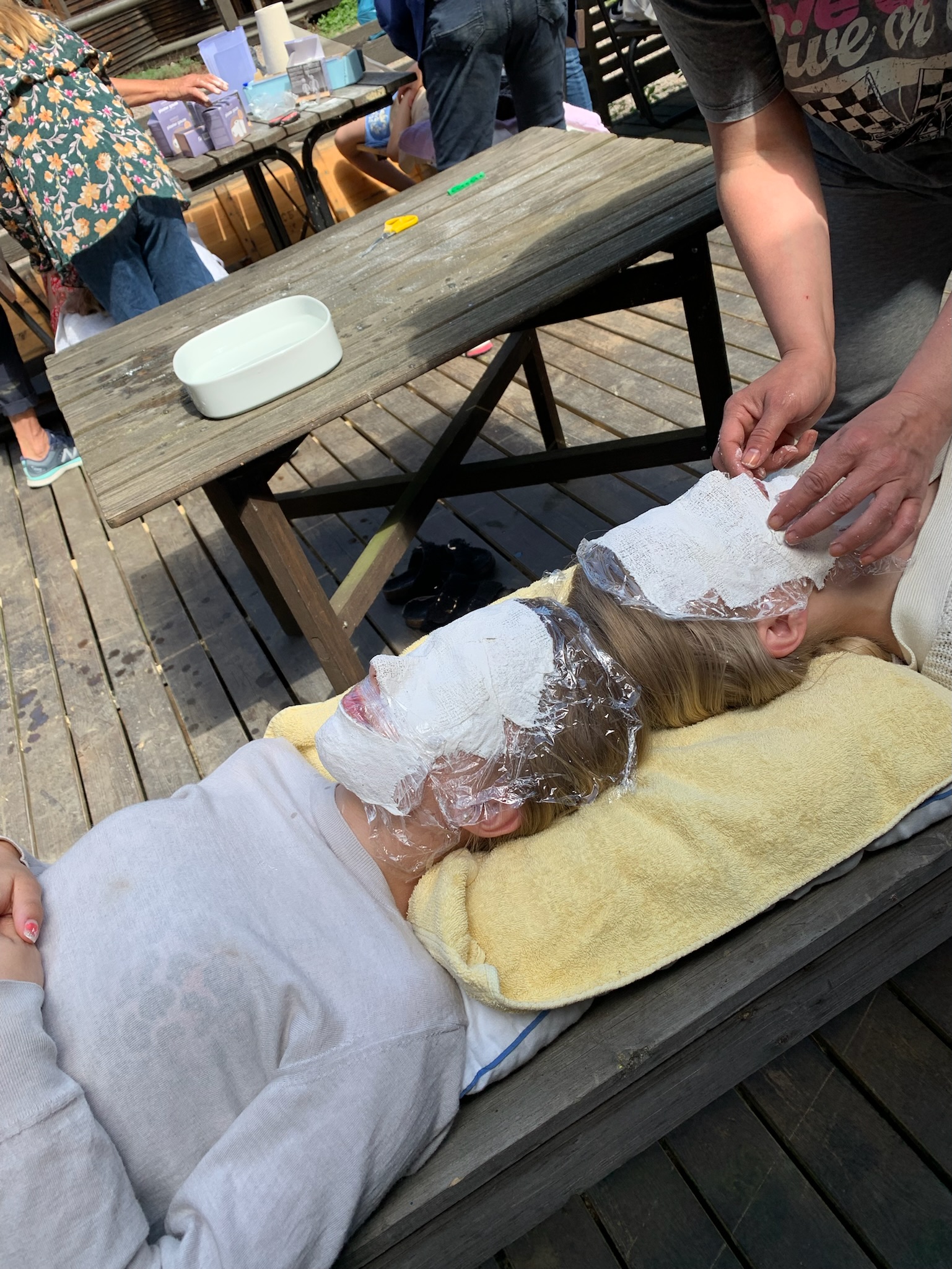 Deltagare får en ansiktsmask av gips vid ett bord utomhus