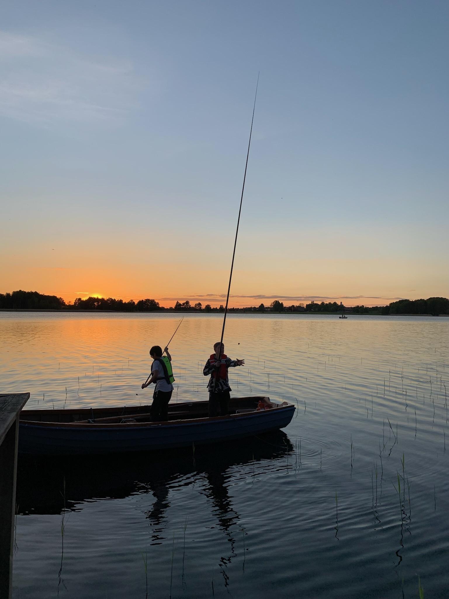 Två personer fiskar från en båt i solnedgången