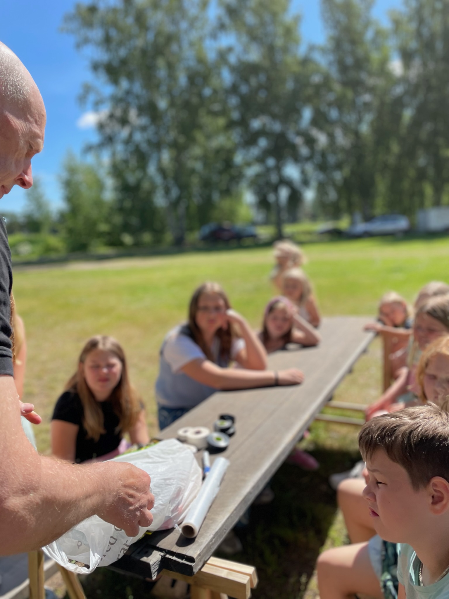 Deltagare följer en demonstration kring ett bord på gräsmattan